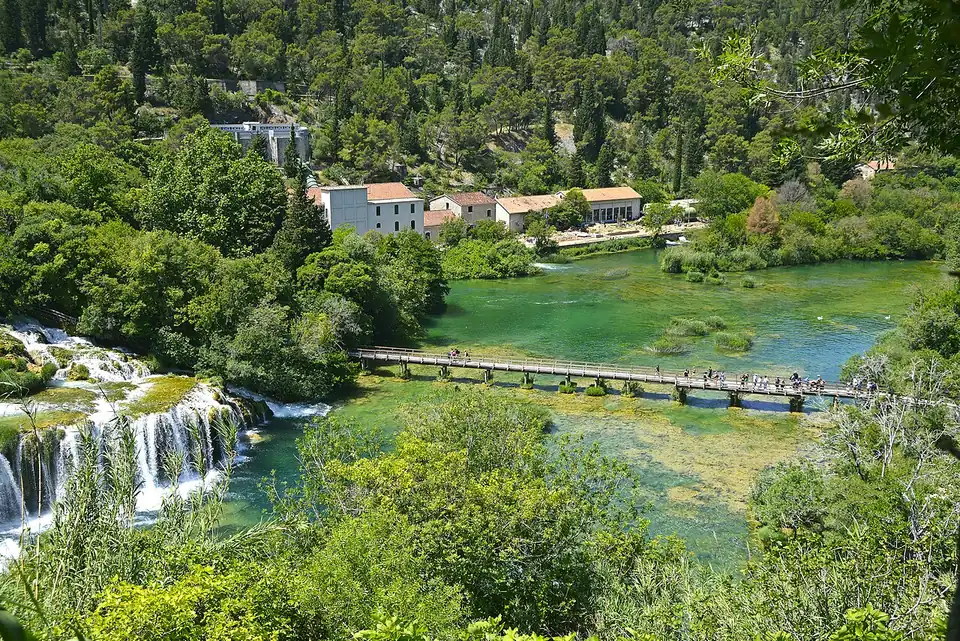 The Skradinski buk waterfalls in Krka National Park, water spilling over green travertine terraces beside a wooden boardwalk and old stone mill buildings