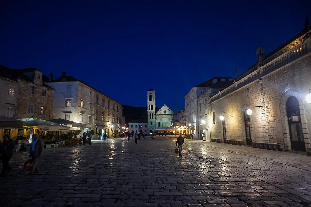 The main square of Hvar town at dusk, the cathedral and bell tower lit up at the end of the wide stone plaza