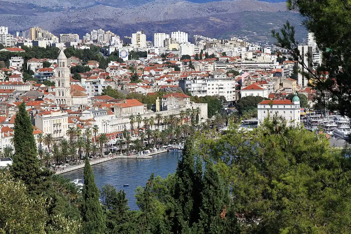 View over the old town of Split from a hillside, the cathedral bell tower rising above terracotta roofs with the palm-lined Riva and harbour below