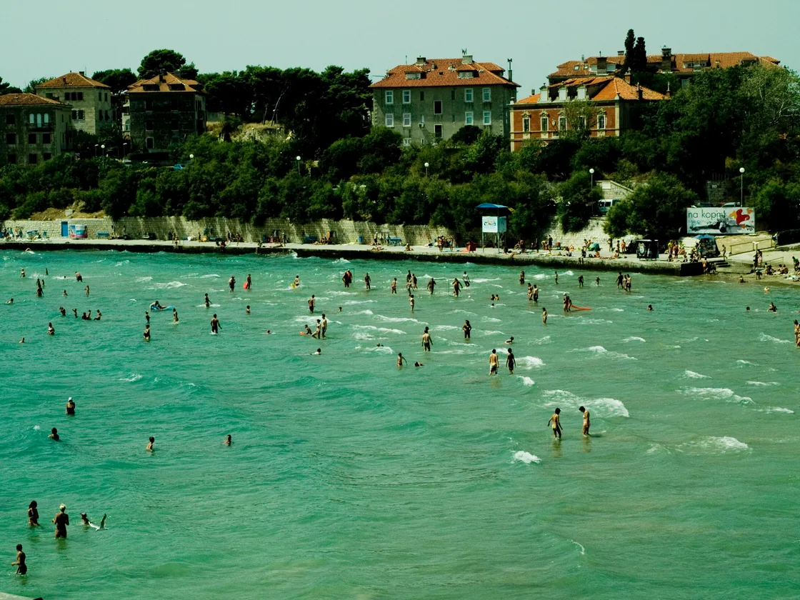 People standing in the shallow turquoise water of Bačvice bay a long way from shore