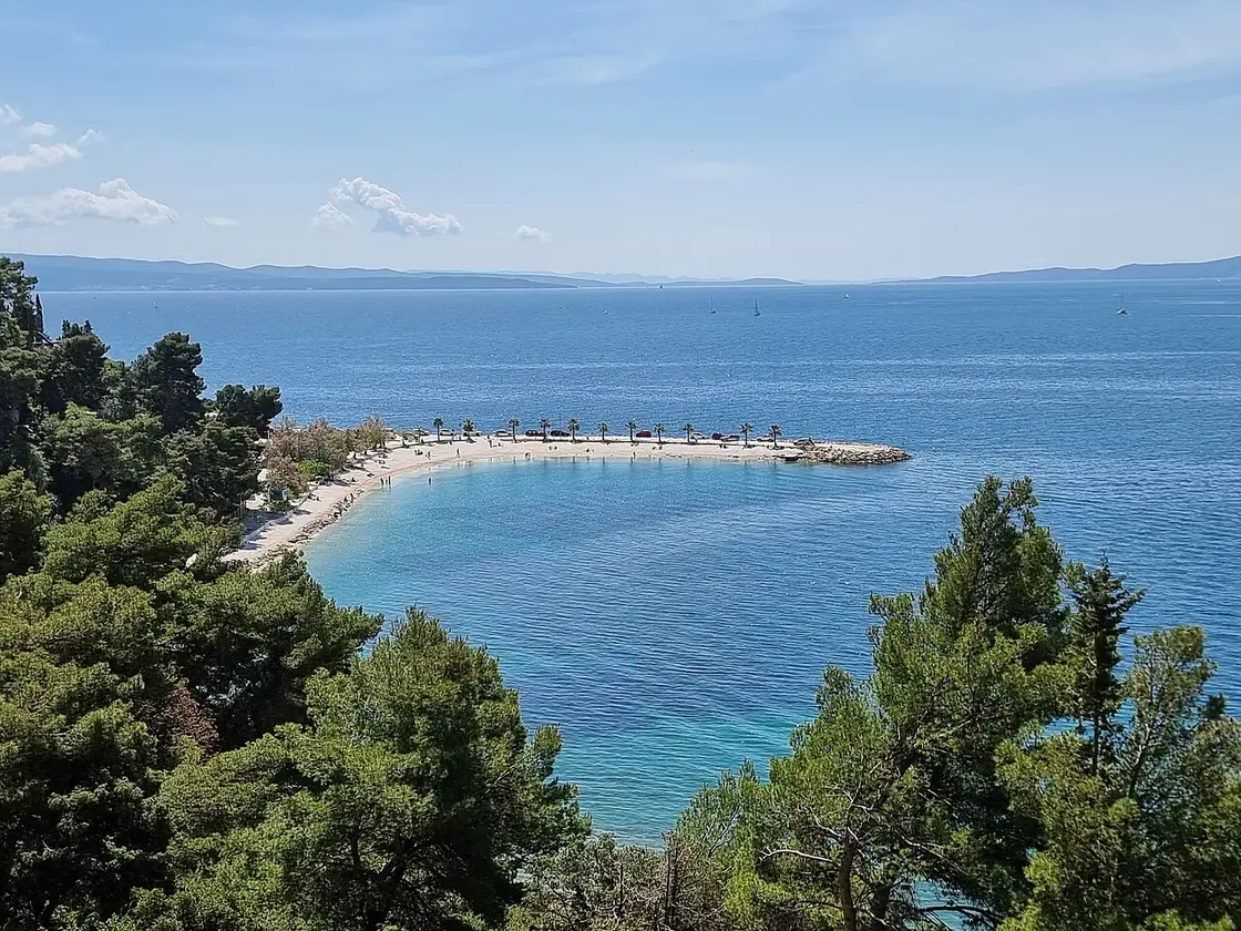 Kašjuni pebble beach on Marjan with calm water and trees on the slope above