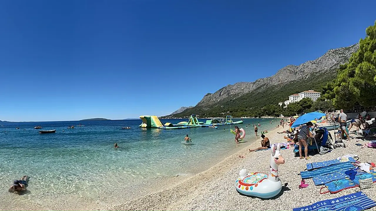 A sunny pebble beach on the Croatian Adriatic in summer with turquoise water and bathers