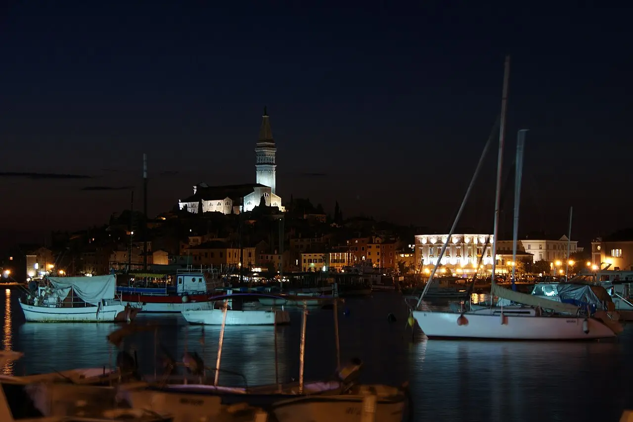 The old town of Rovinj in Istria lit up after sunset with boats in the harbour