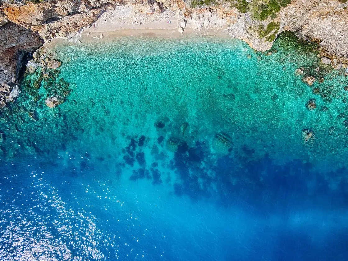 An aerial view of a turquoise Adriatic cove below limestone cliffs in summer