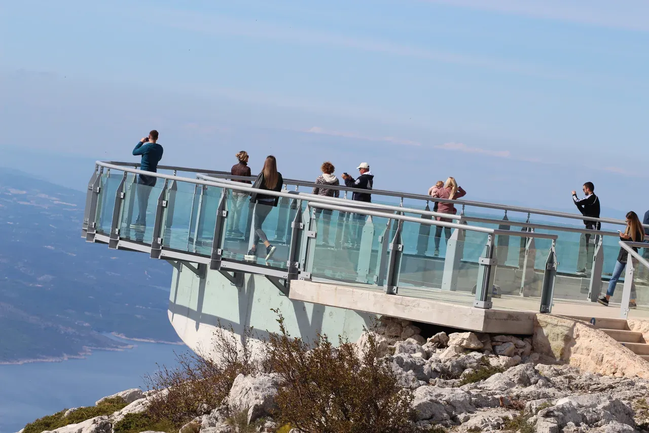 Visitors on the semicircular glass Biokovo Skywalk platform jutting out over the cliff, with the Adriatic far below