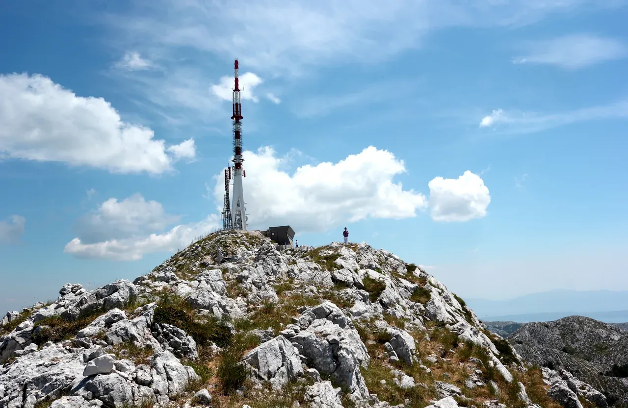 The rocky summit of Sveti Jure, the highest peak of Biokovo at 1,762 m, with its transmitter tower and a lone hiker