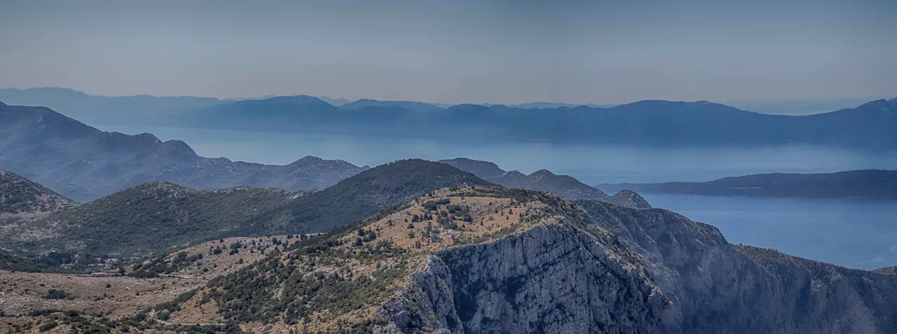 A wide panorama from high on Biokovo over rolling karst ridges to the Adriatic islands in the haze