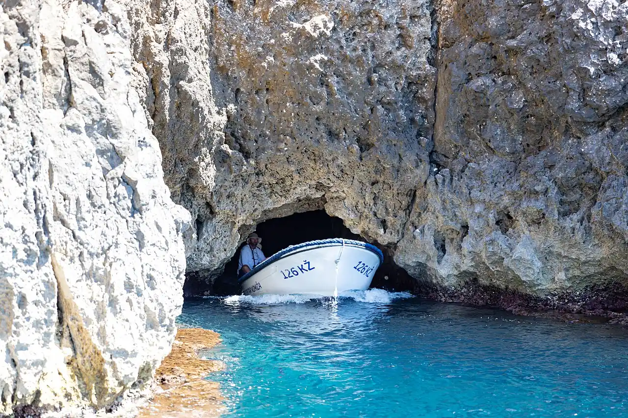 A small tour boat squeezing through the low rock entrance of the Blue Cave on Biševo, the arch barely higher than the passengers
