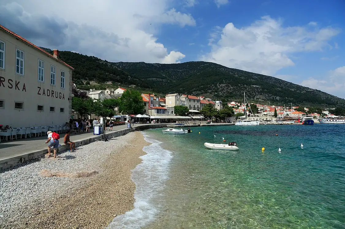 The stone waterfront and harbour of Bol on Brač, with boats moored and the mountain behind
