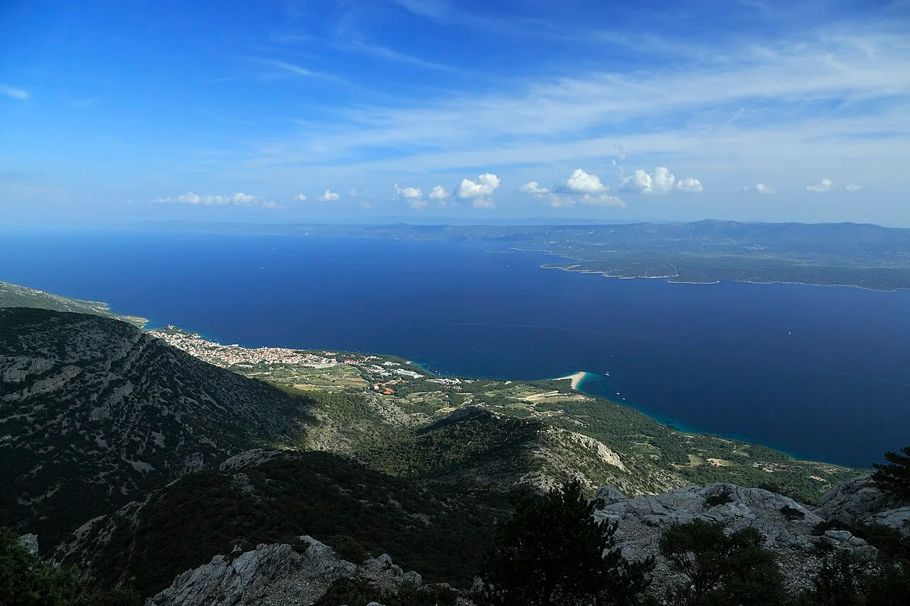 Aerial view of the Zlatni Rat spit on Brač reaching into the blue Adriatic, with the island of Hvar on the horizon