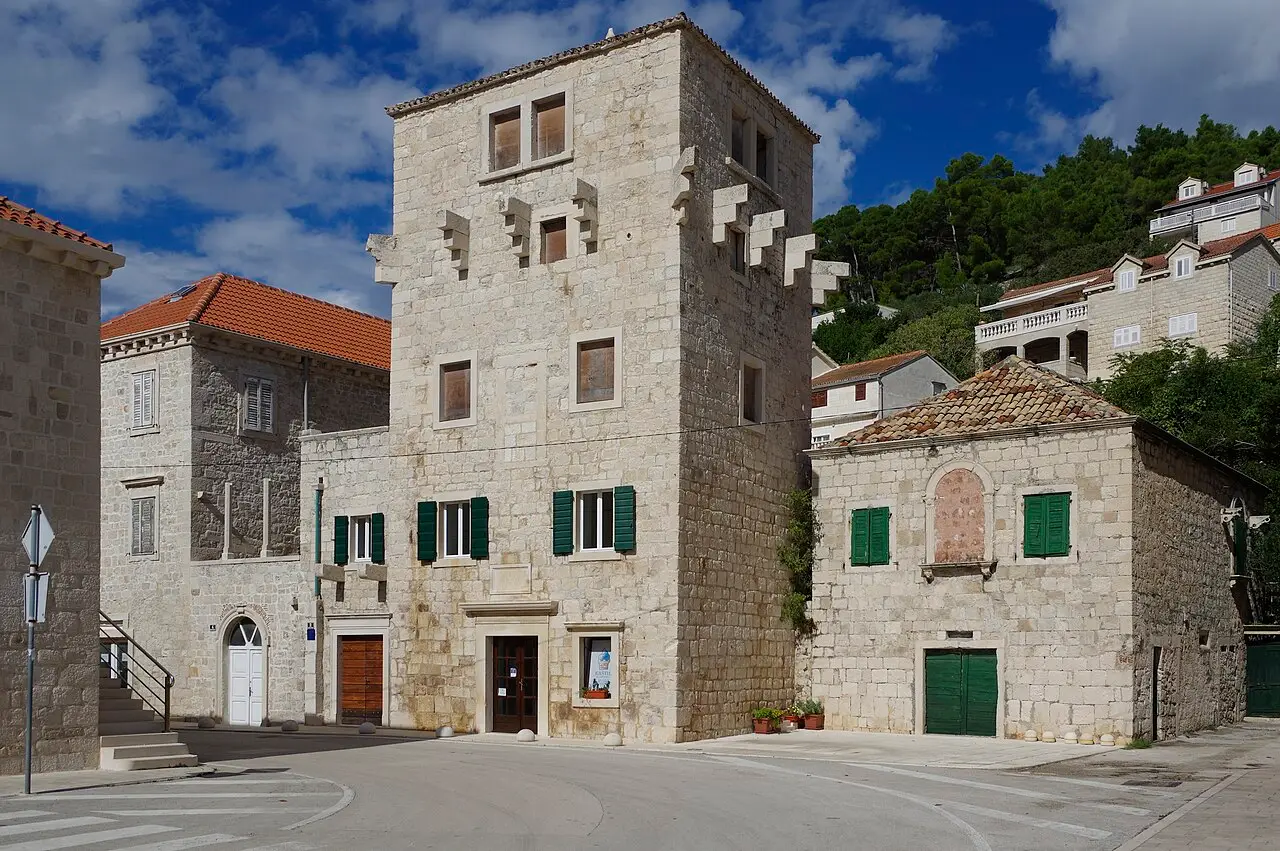 Stone houses and a quay of white Brač limestone in Pučišća reflected in the calm bay