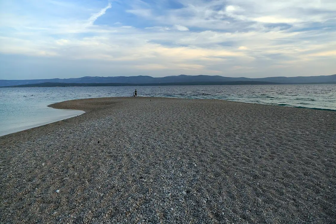 The pointed tip of the Zlatni Rat spit on Brač, curving to one side, seen from above with windsurfers in the water