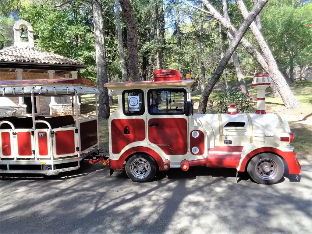 The red and cream tourist train that carries visitors around Veliki Brijun, parked under pines beside a small chapel
