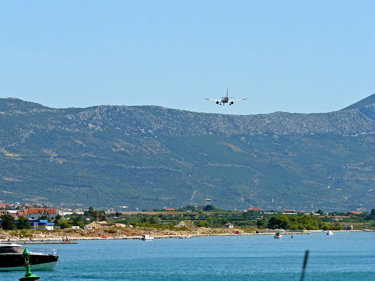 A jet on final approach over Kaštela bay toward Split Airport, with the Kozjak mountain ridge behind