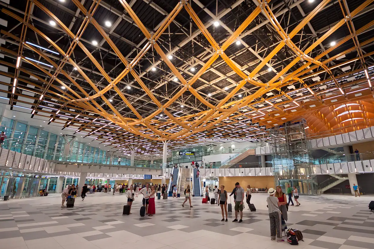 The sweeping wooden-slatted ceiling of Split Airport's main hall, with travellers and rolling suitcases below the departure boards
