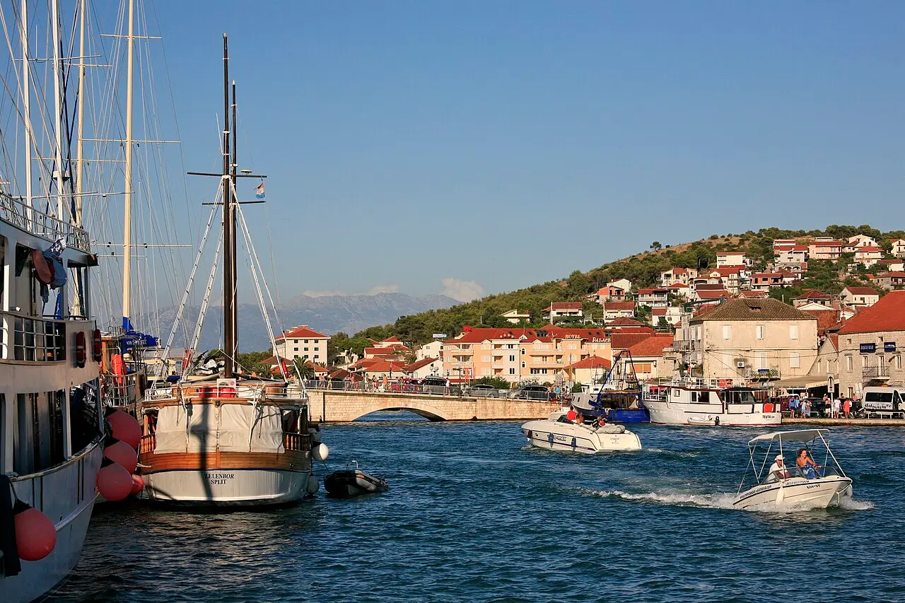 Boats on the channel at Trogir with the stone old town and its bridge, and a wooded hillside of houses behind