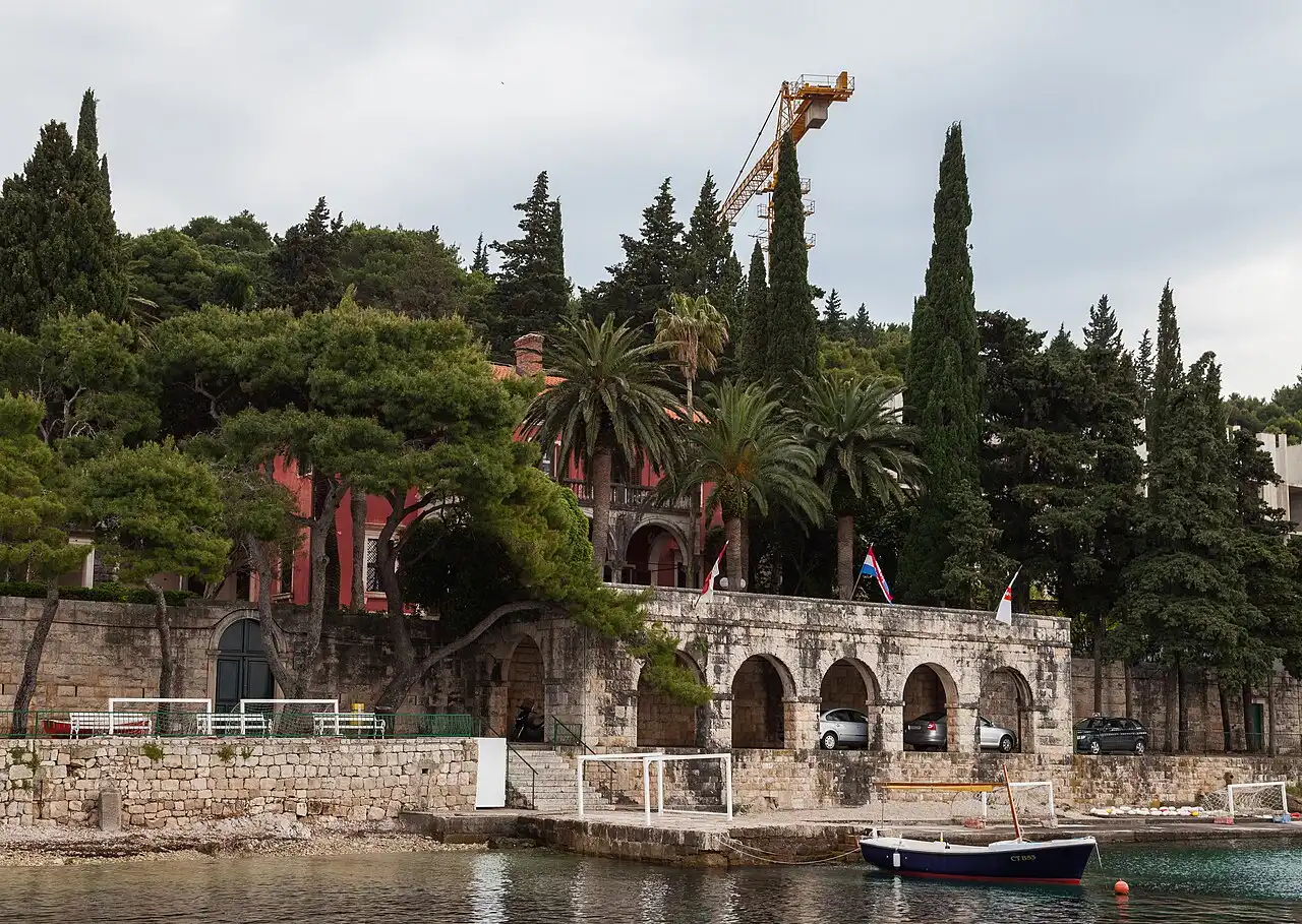 Stone arcade and waterfront wall at Cavtat under an overcast sky, a small boat moored below