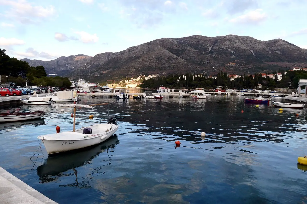 Moored boats in Cavtat harbour at dusk, with the bare limestone ridge rising behind the town