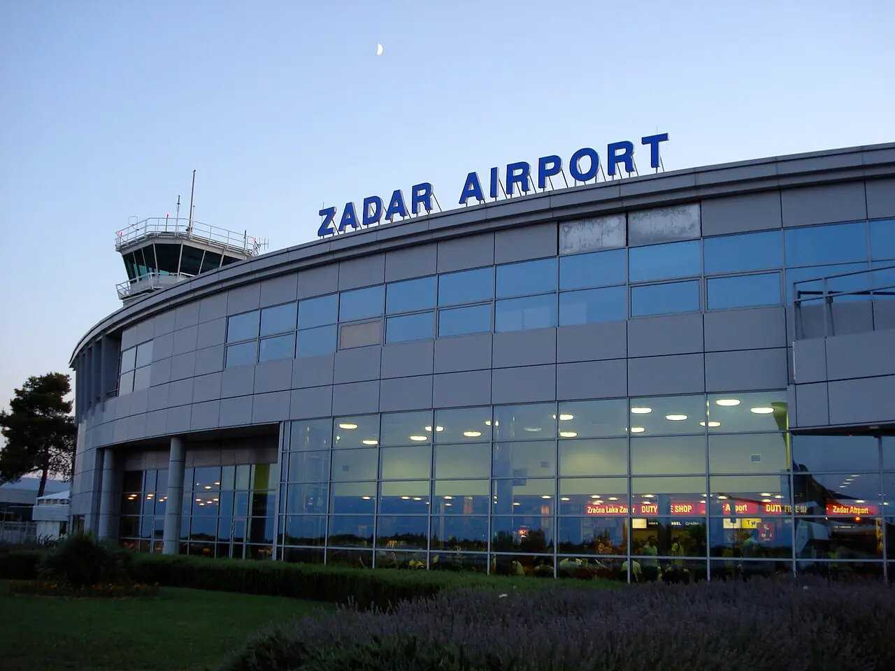 The glass terminal building of Zadar Airport at dusk with the control tower behind
