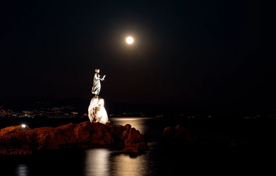 The Maiden with the Seagull statue on its rock in Opatija under a full moon at night