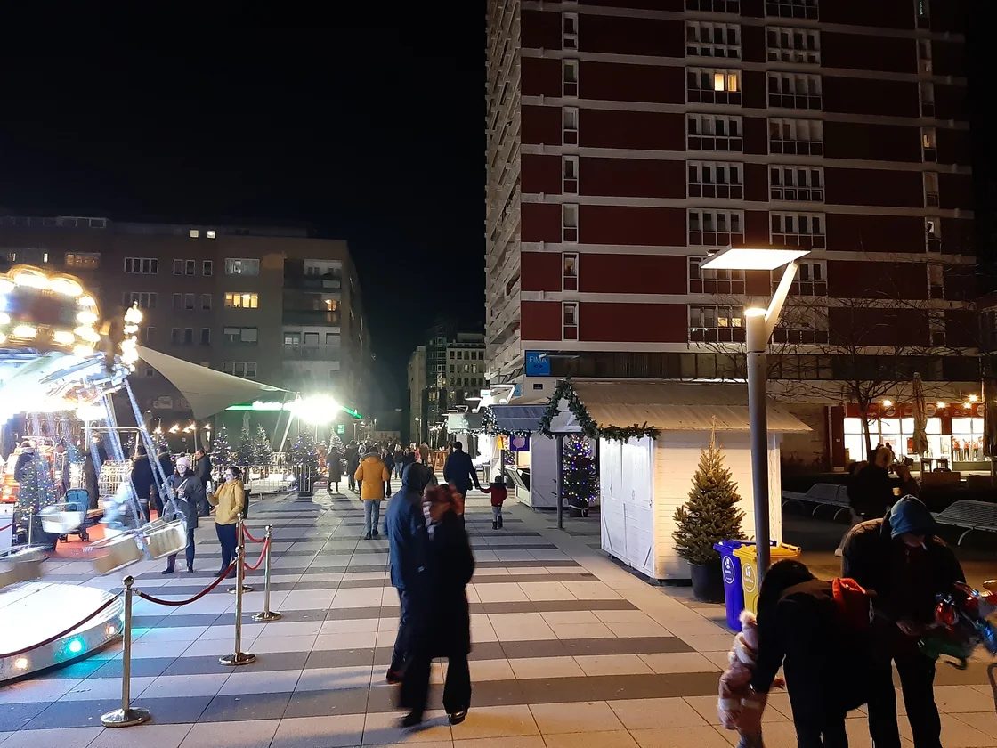 A lit carousel on a pedestrian square in Osijek in the evening with people around it