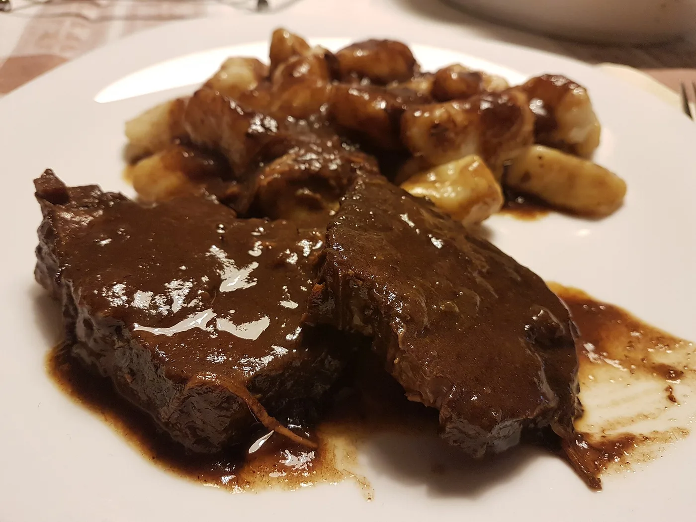A plate of Dalmatian pašticada, sliced braised beef in dark sauce served with gnocchi