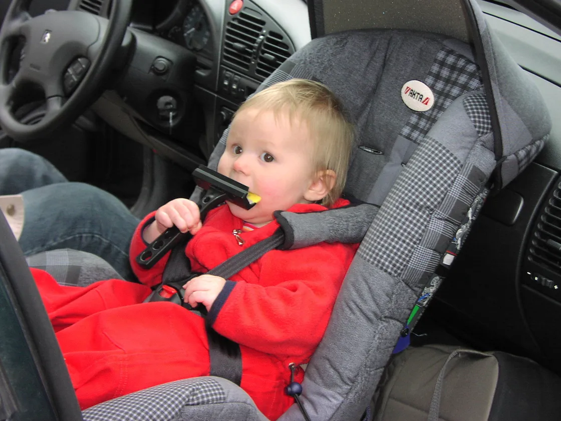 A rear-facing infant car seat installed in the front passenger seat of a car, with a baby strapped in