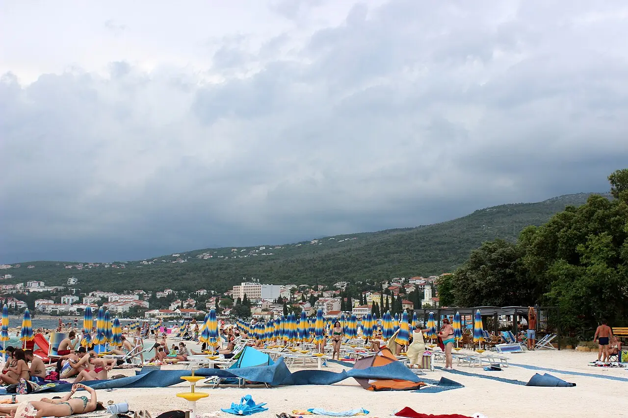 Rows of rented sunbeds and umbrellas on a beach at Selce beside clear Adriatic water
