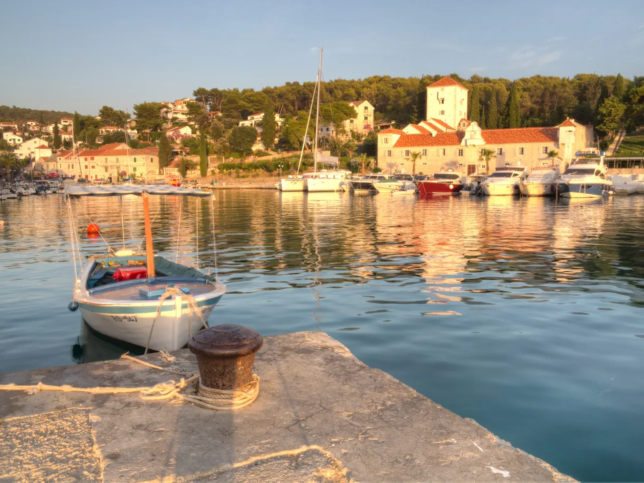 The calm harbour of Maslinica on the island of Šolta at golden hour, with fishing boats and a stone church