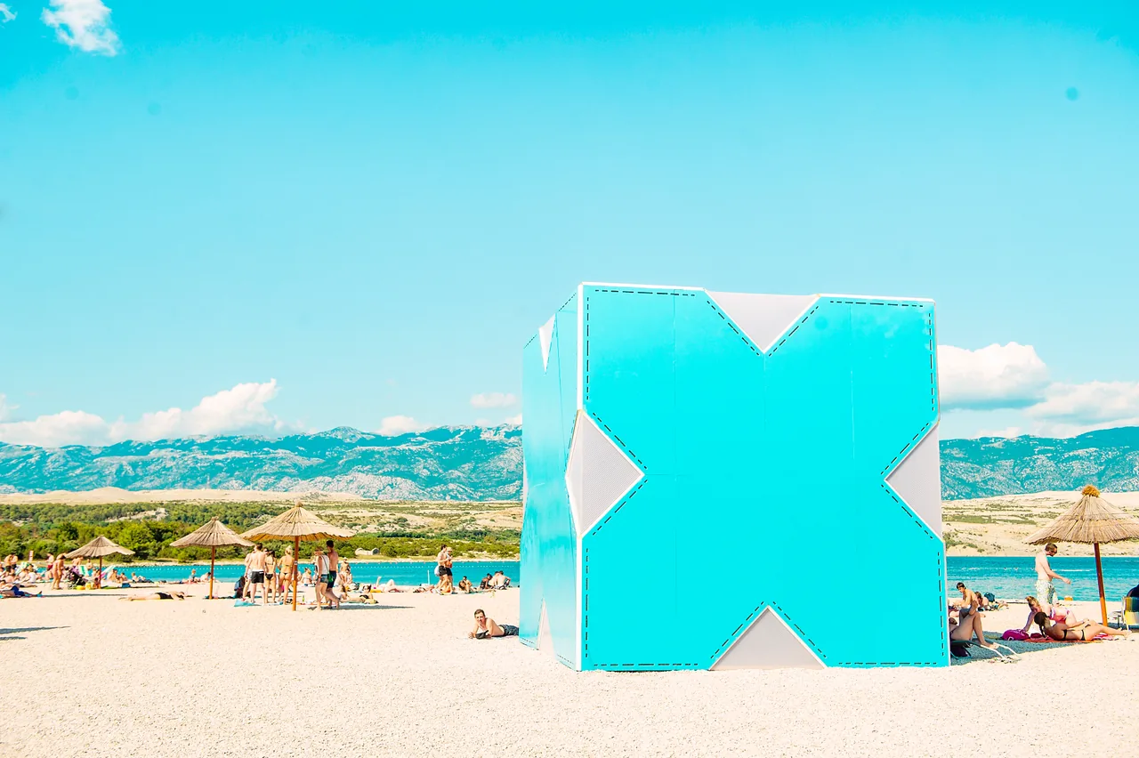 Zrće beach on the island of Pag on a sunny day, with sunbathers, thatched parasols and beach-club structures