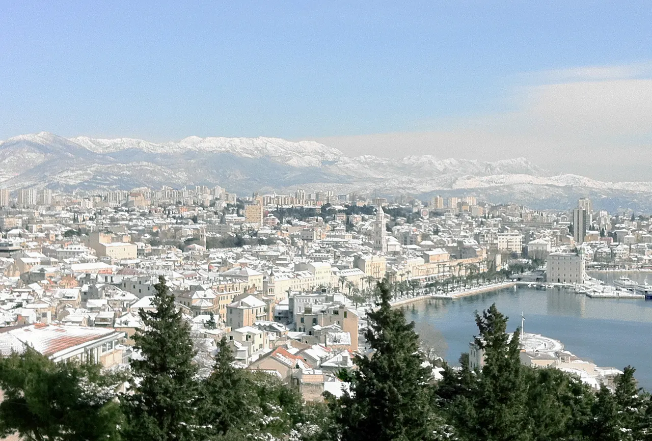 Split under snow seen from Marjan hill, with white rooftops, the harbour and snowy mountains behind the city