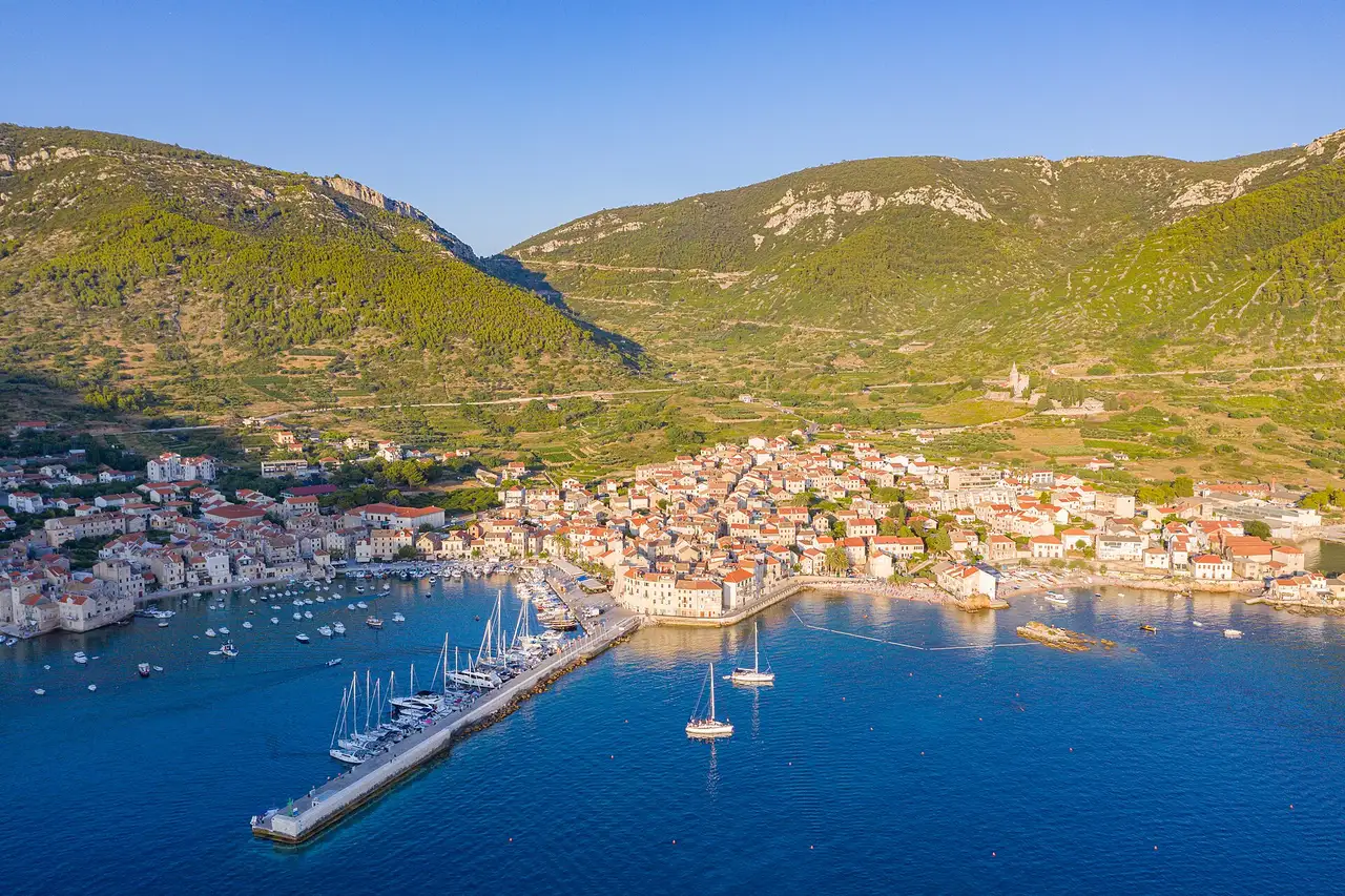 Aerial view of Komiža harbour on Vis island, boats in the marina and stone houses backed by green hills