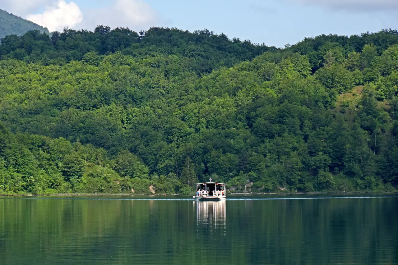 A tourist boat crossing the green lakes of Plitvice among wooded hills