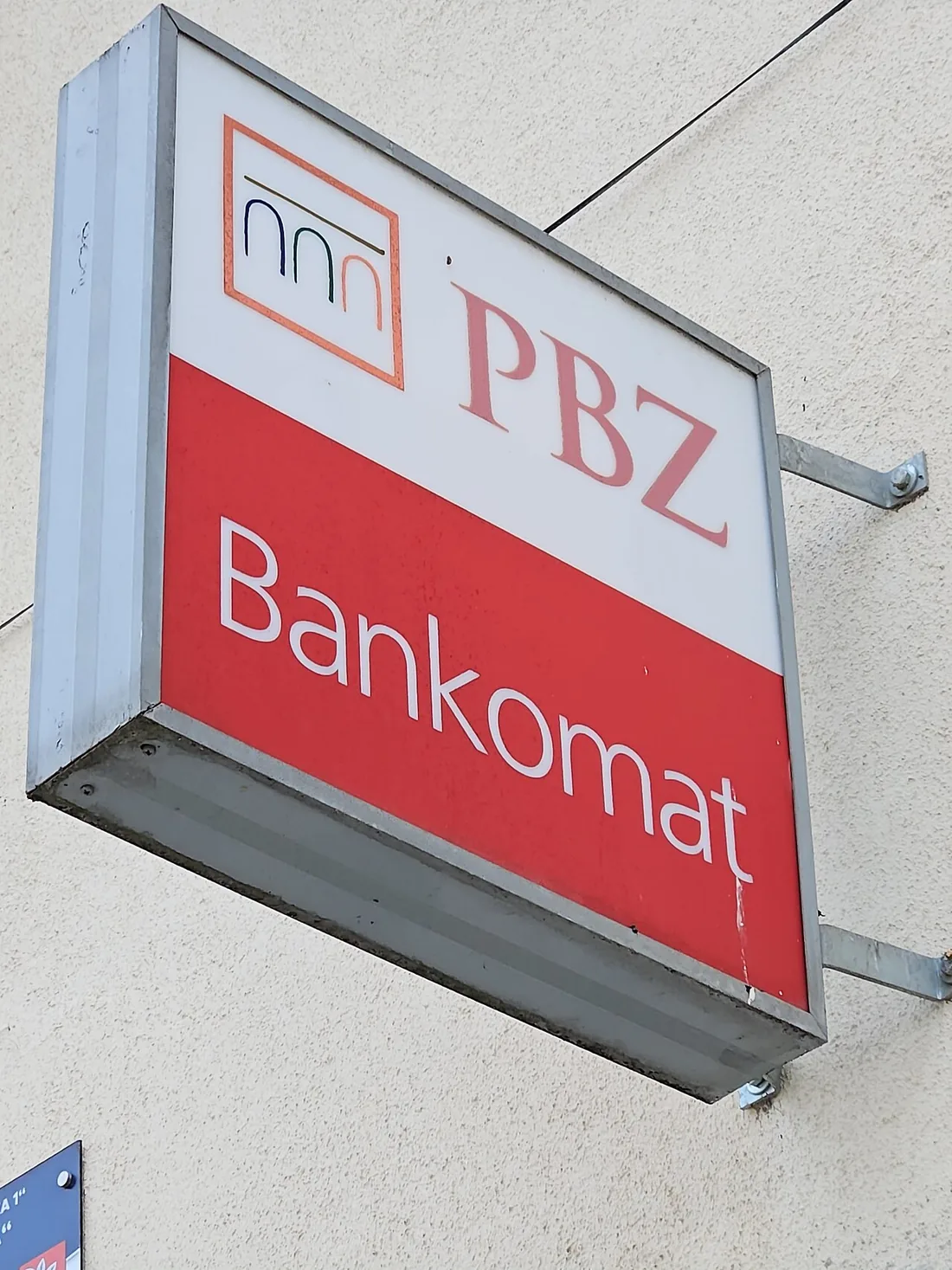 A red and white PBZ Bankomat sign mounted on a wall, marking a Croatian bank ATM