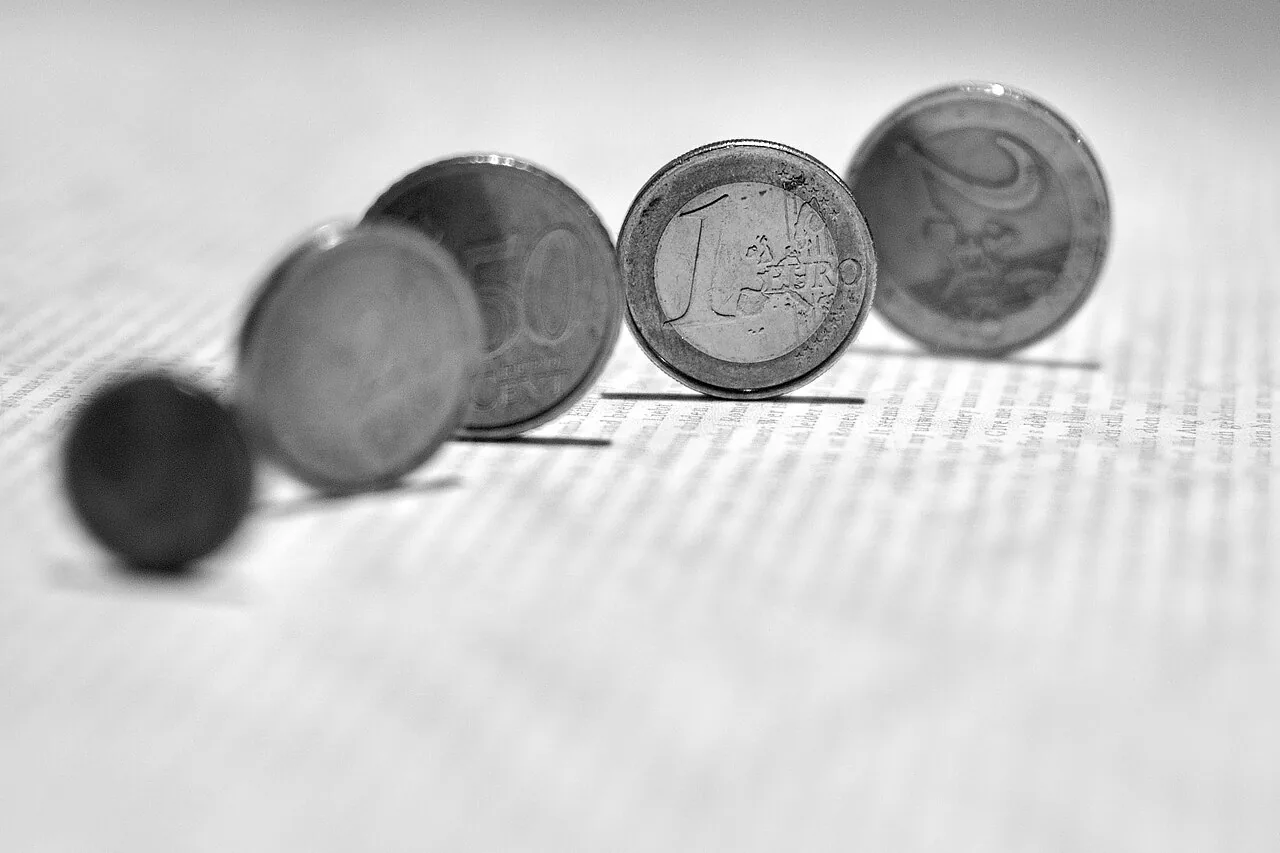 Close-up of several euro coins, including a one-euro coin, standing on a printed page