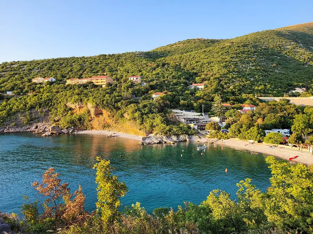 A green Croatian cove with a small pebble beach and almost no shade at the waterline