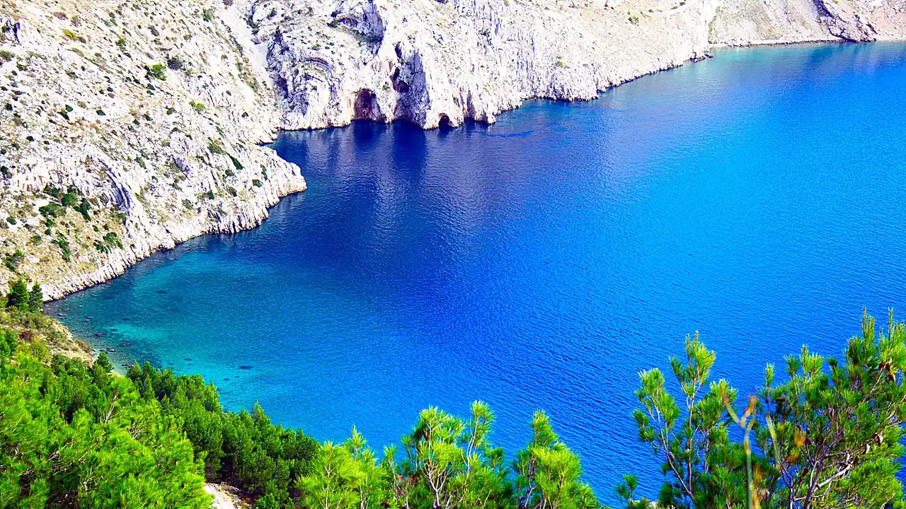 A hidden turquoise cove backed by white cliffs and pines on the Dalmatian coast between Omis and Makarska