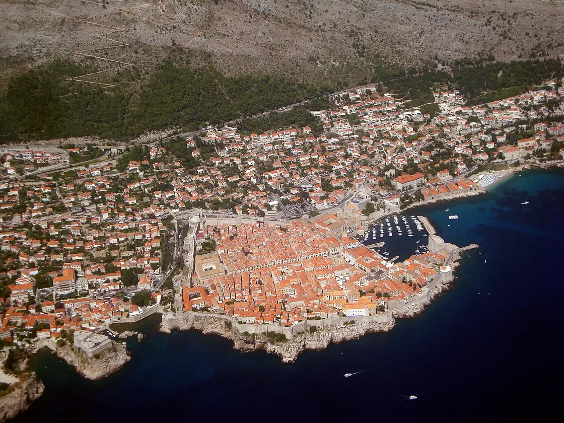 Aerial view of the walled Old Town of Dubrovnik on its rocky point, terracotta roofs and the harbour below green hills