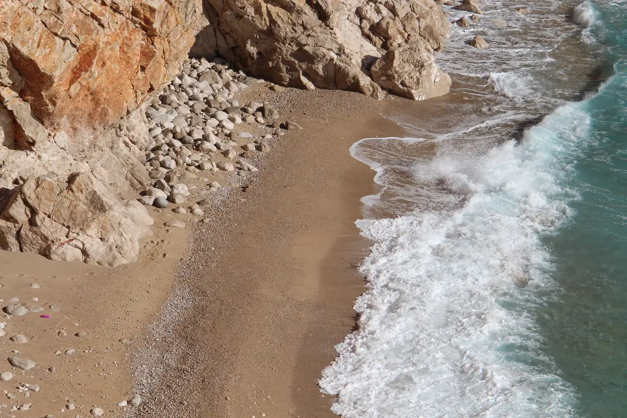 A cliff-backed sandy beach at Pasjača in southern Croatia with clear turquoise Adriatic water breaking on the shore