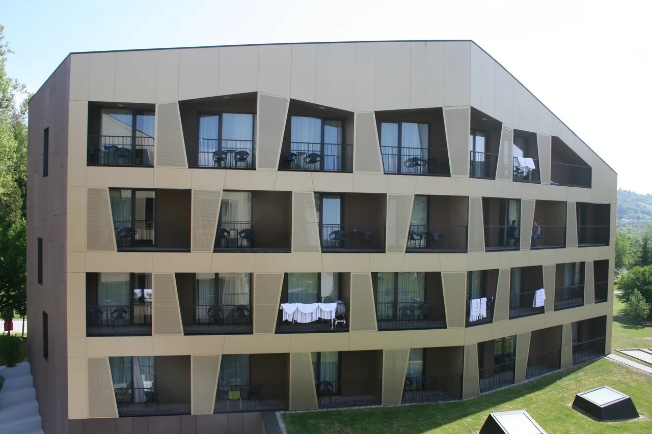 The angular four-storey facade of Hotel Well at Terme Tuhelj, with balconies over a lawn and the Zagorje hills behind