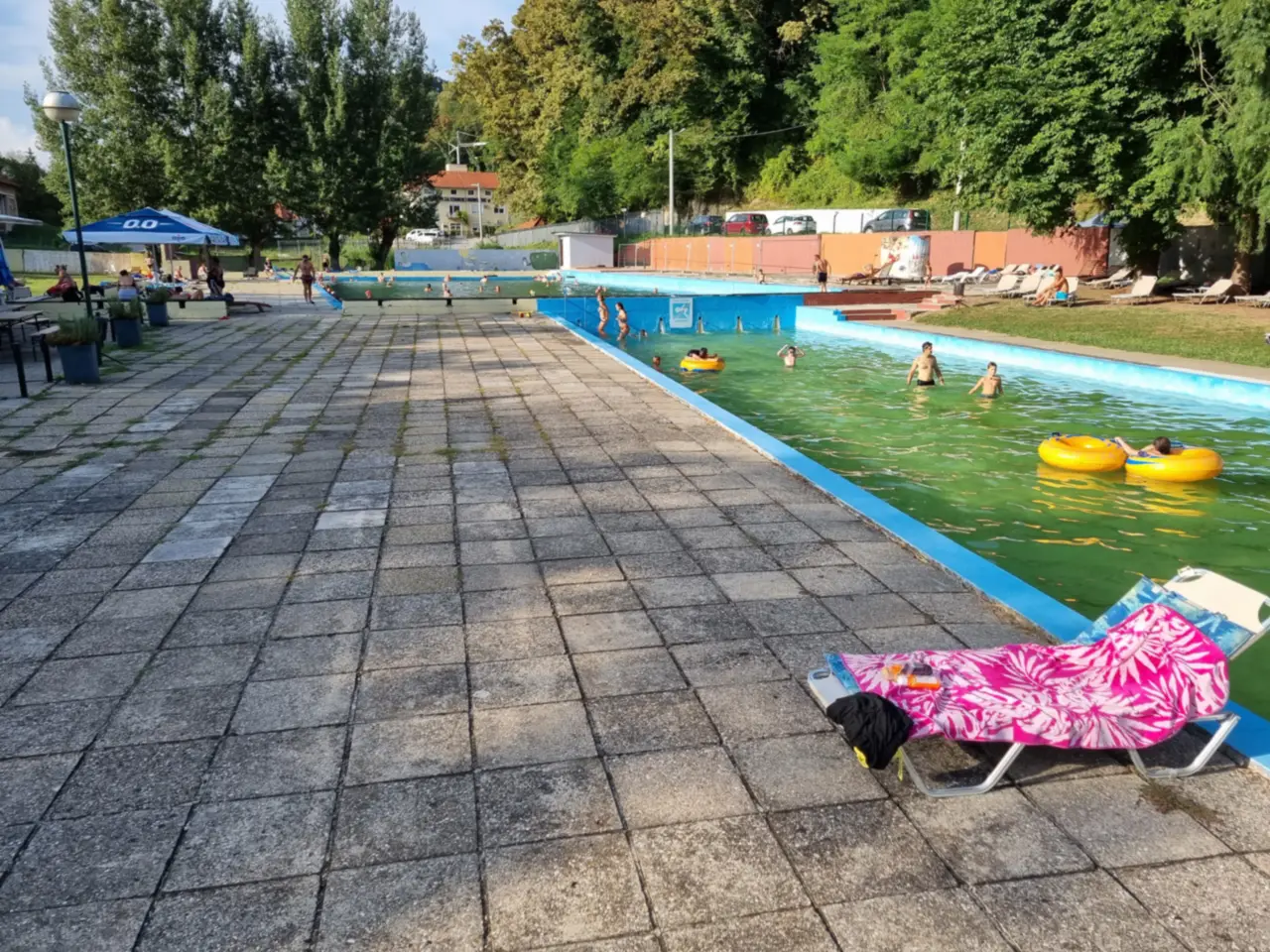 The old outdoor pools at the spring at Terme Tuhelj in summer, with swimmers, rubber rings and sun loungers under tall trees
