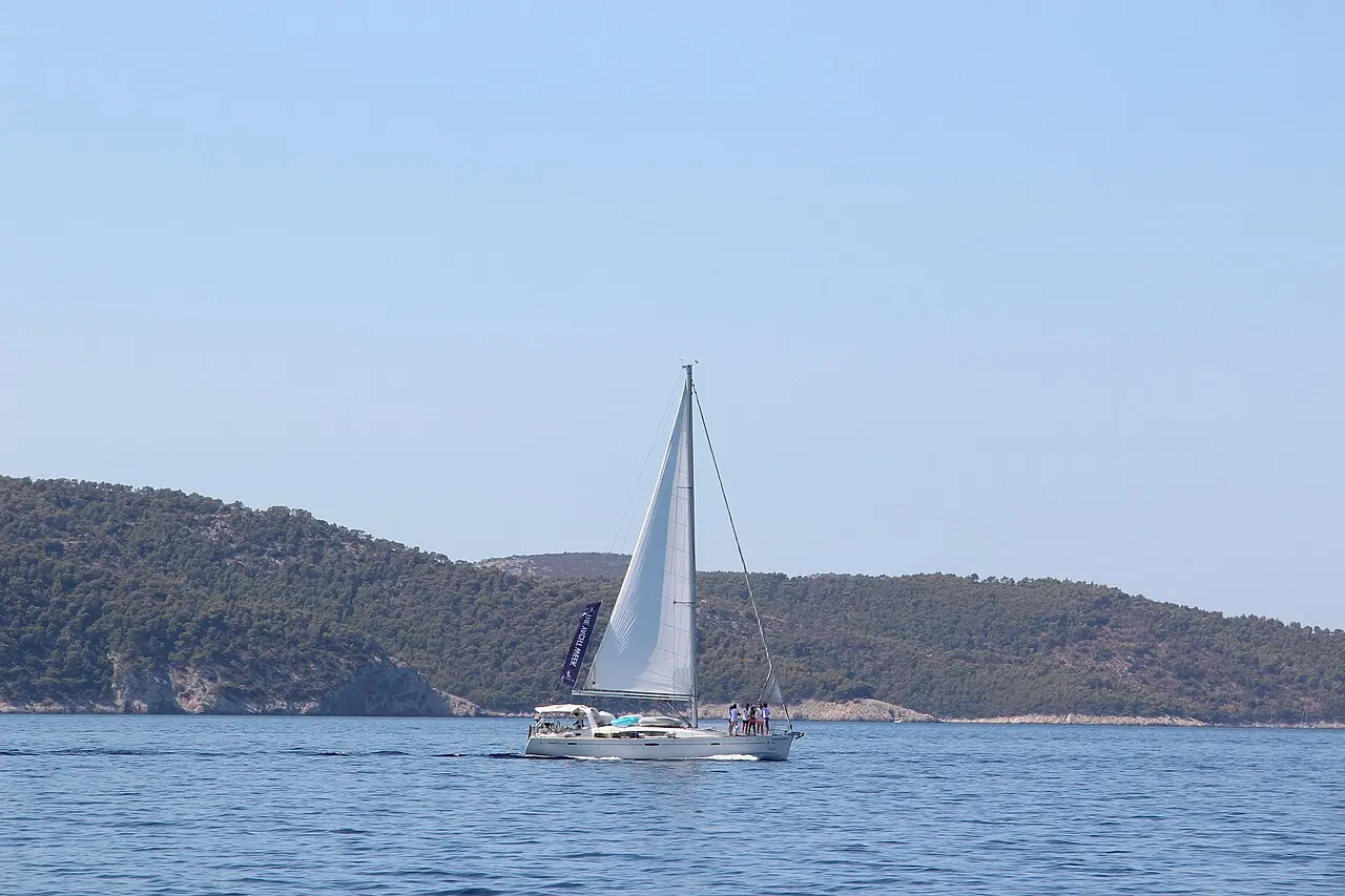A sailing yacht with crew cruising off the wooded Dalmatian coast, Croatia