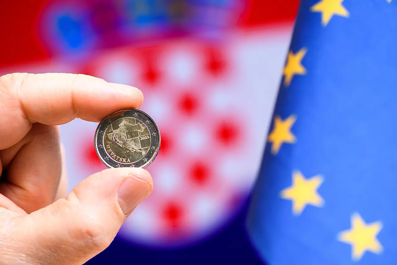 A Croatian 2-euro coin held up against the Croatian and EU flags