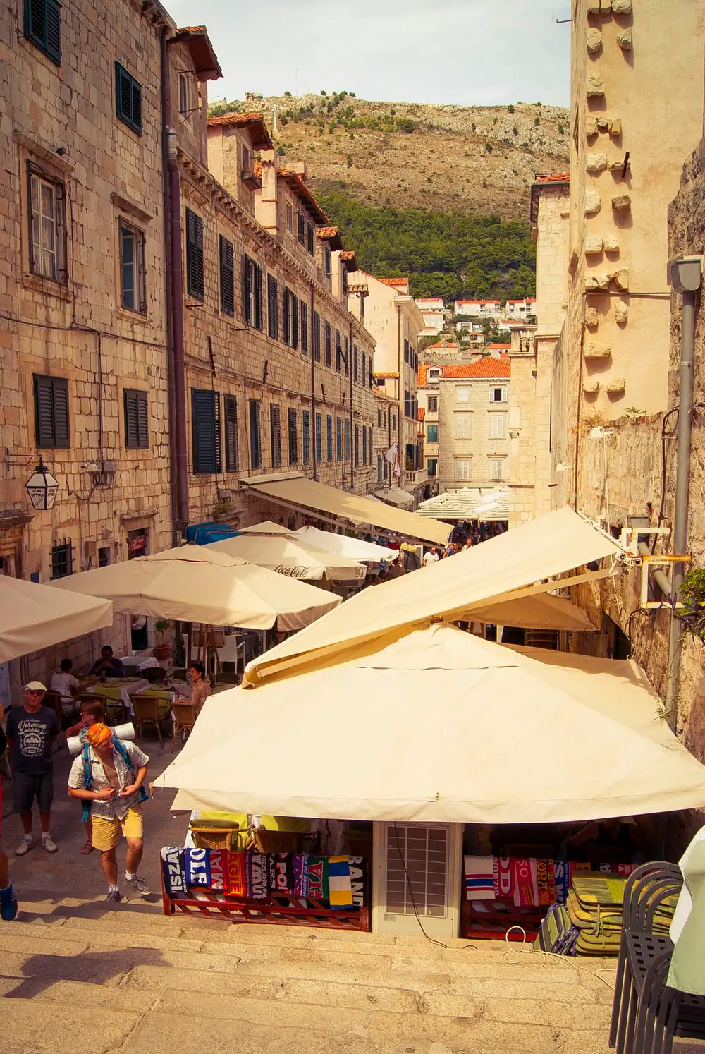 A stepped lane in Dubrovnik old town lined with café parasols and a market stall