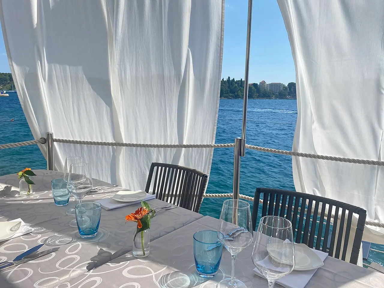 A laid restaurant table with wine glasses on a seaside terrace overlooking the Adriatic