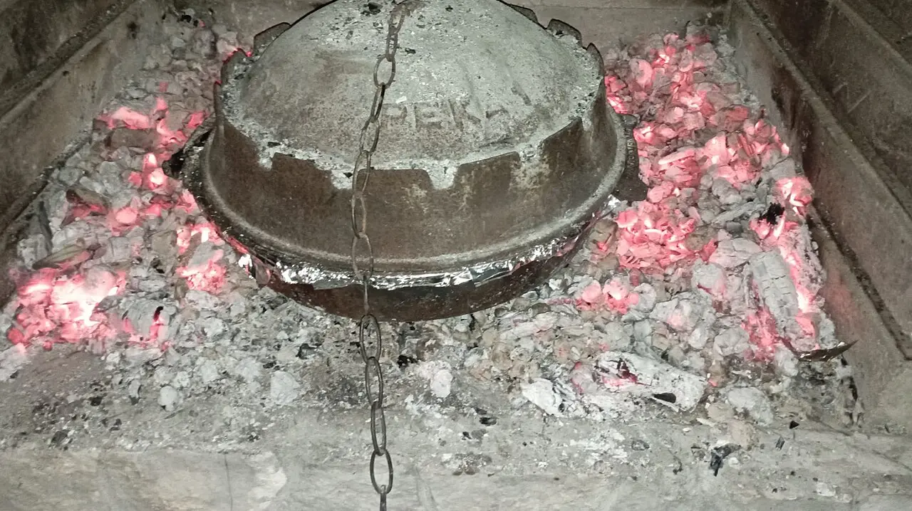 A cast-iron peka bell sitting in glowing embers inside a stone fireplace