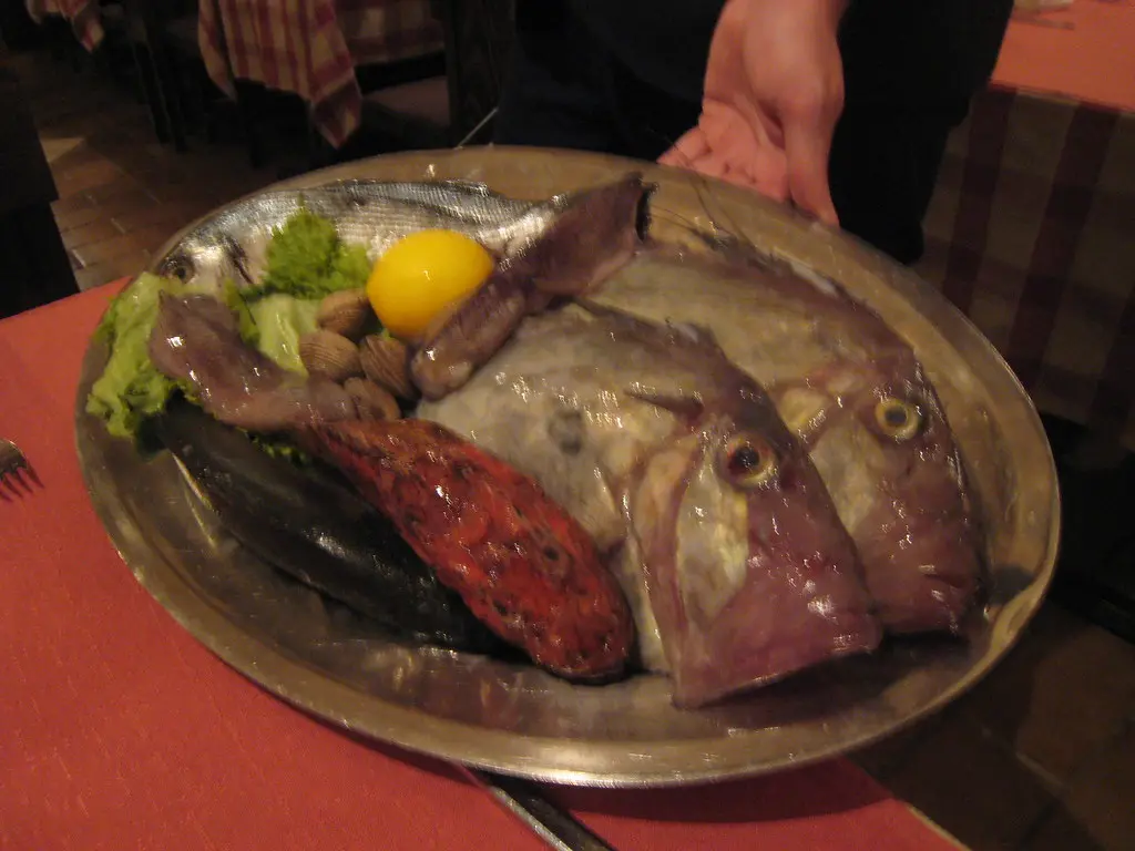 A waiter presenting a metal tray of whole fresh fish to a table in a Split konoba