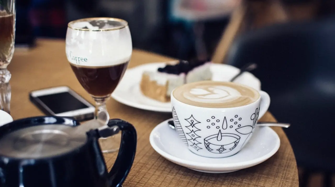 A cappuccino with latte art and a slice of cake on a cafe table