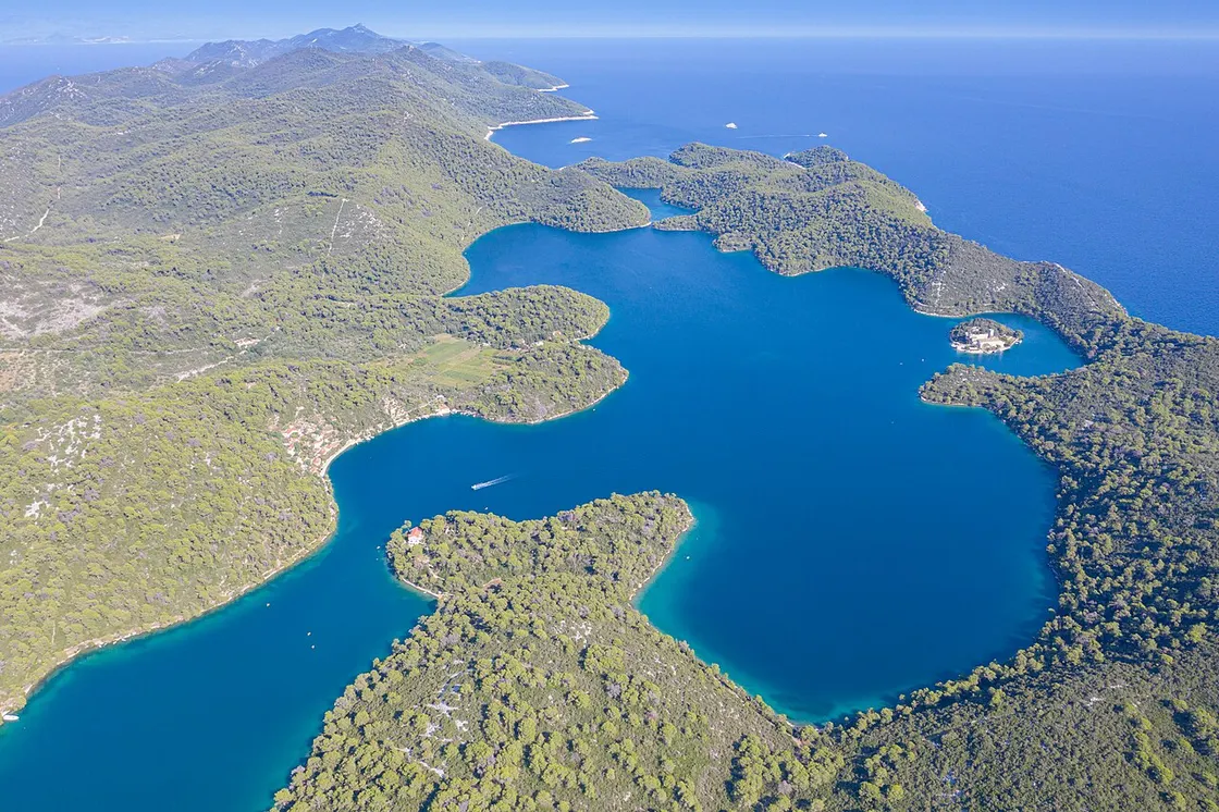 Aerial view of Mljet's two connected saltwater lakes ringed by dense pine forest, with the monastery islet and the open Adriatic behind