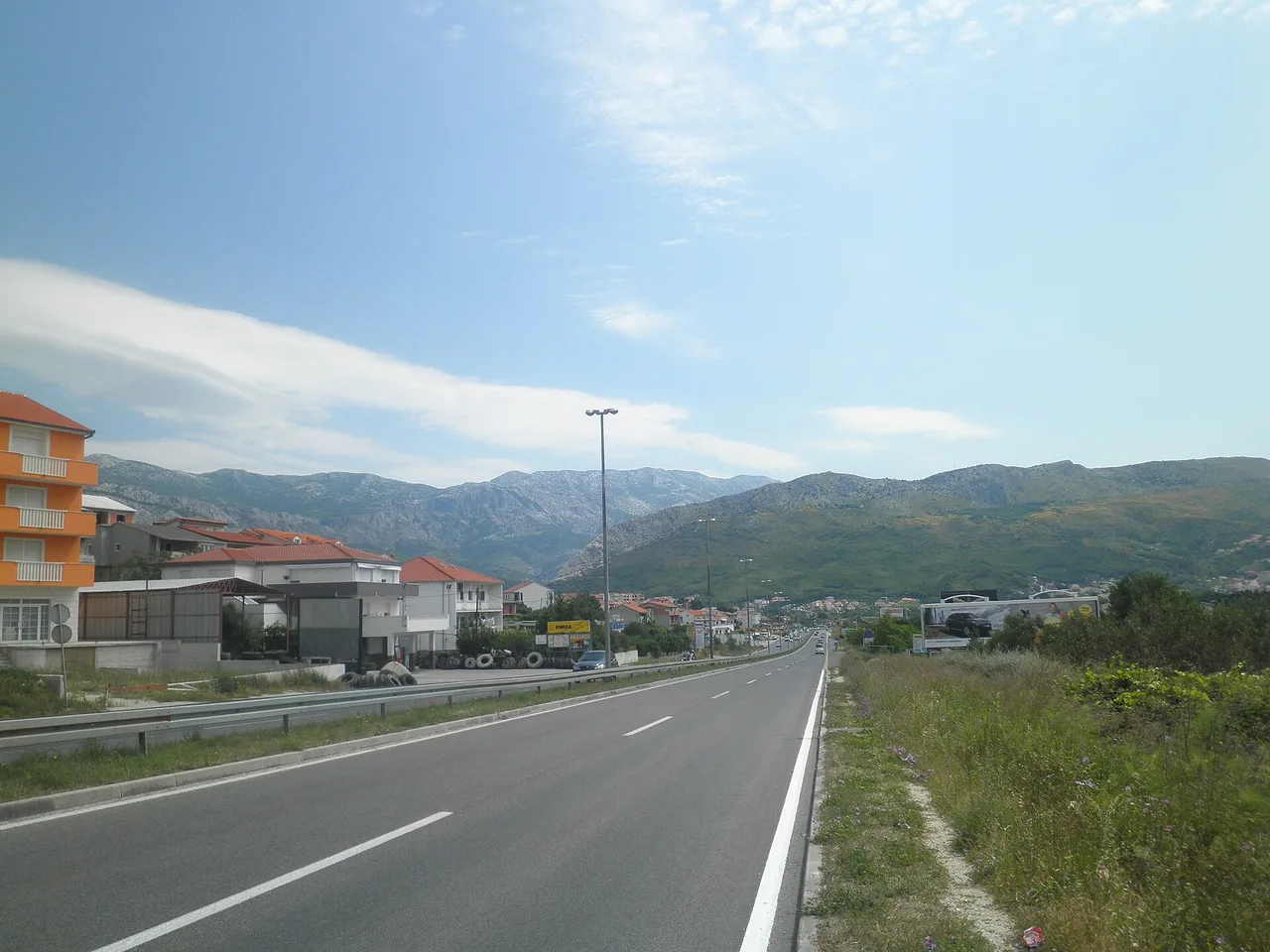 The D8 Adriatic coastal road winding along the sea east of Split under dry hills